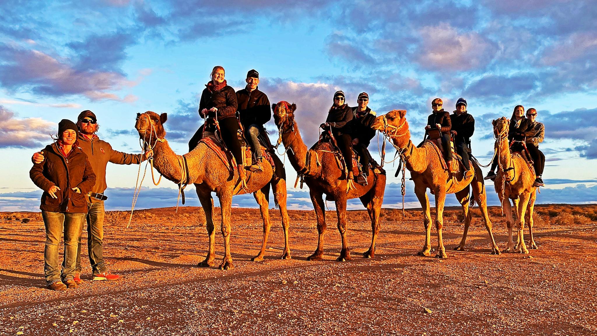 A group of eight people smiling as they enjoy a Silverton Sunset tour with Silverton Outback Camels.