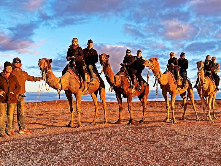 A group of eight people smiling as they enjoy a Silverton Sunset tour with Silverton Outback Camels.