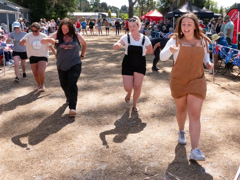 Women in an egg-and-spoon race at an outdoor event, smiling and focused.