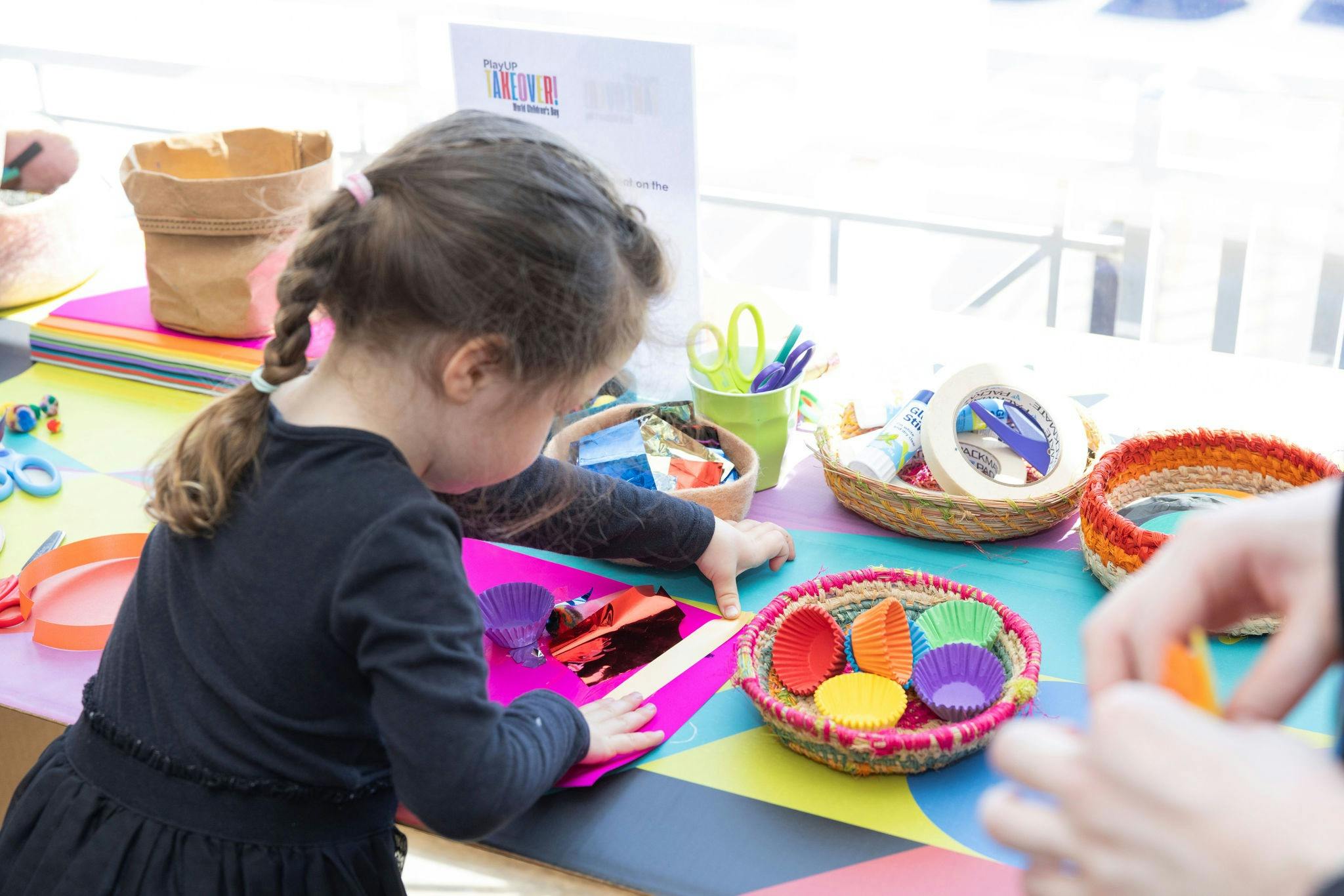 A young girl busy at a crafting table with colourful art supplies.