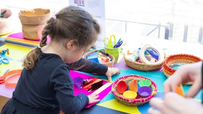 A young girl busy at a crafting table with colourful art supplies.