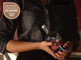 Bar person holding a bottle of Quandong Gin with Bronze Medalist 2021 label