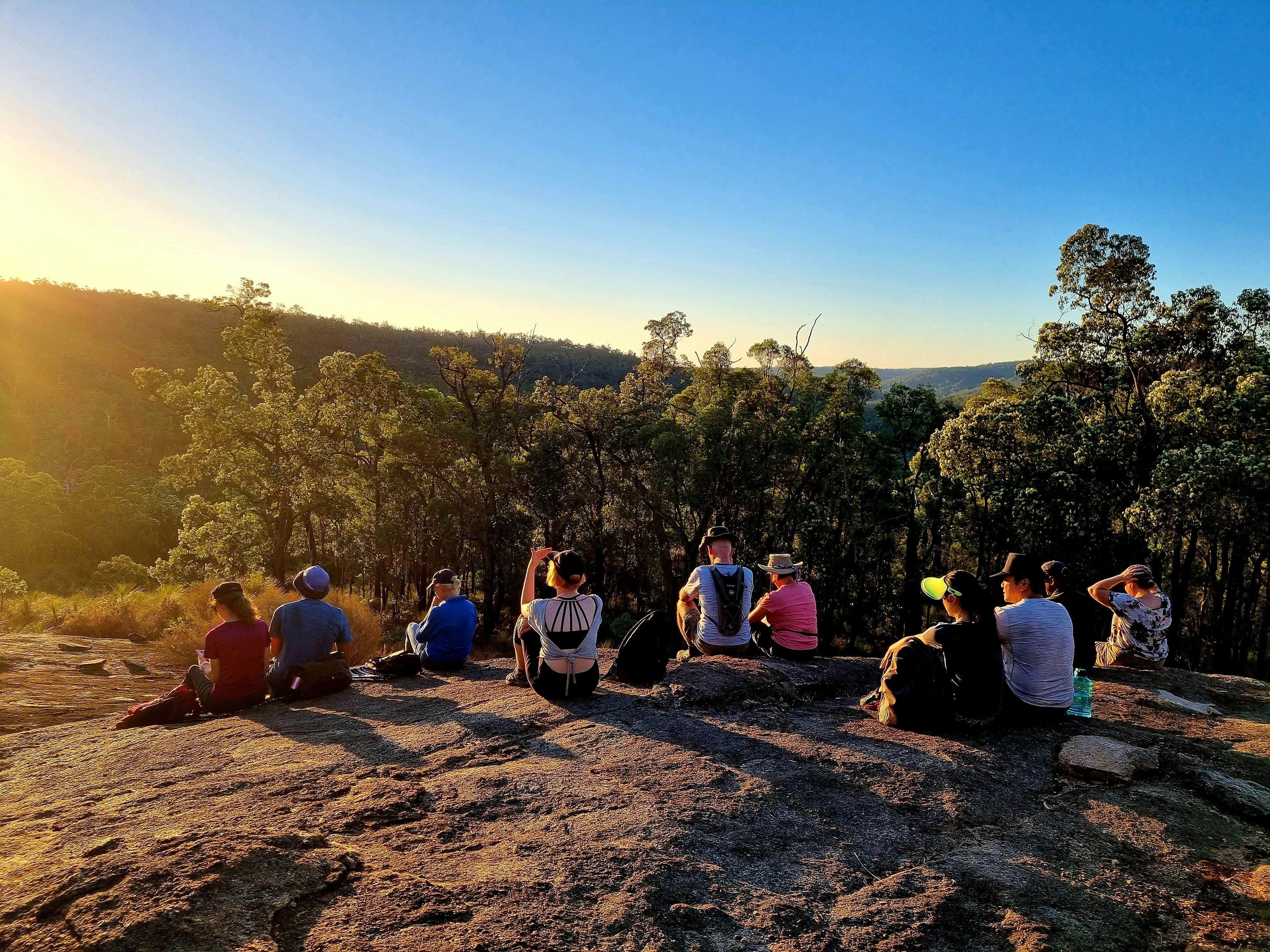 Hikers sitting on rocky hill as they all watch the sun go down. Beautiful blue sky and warm sun hues