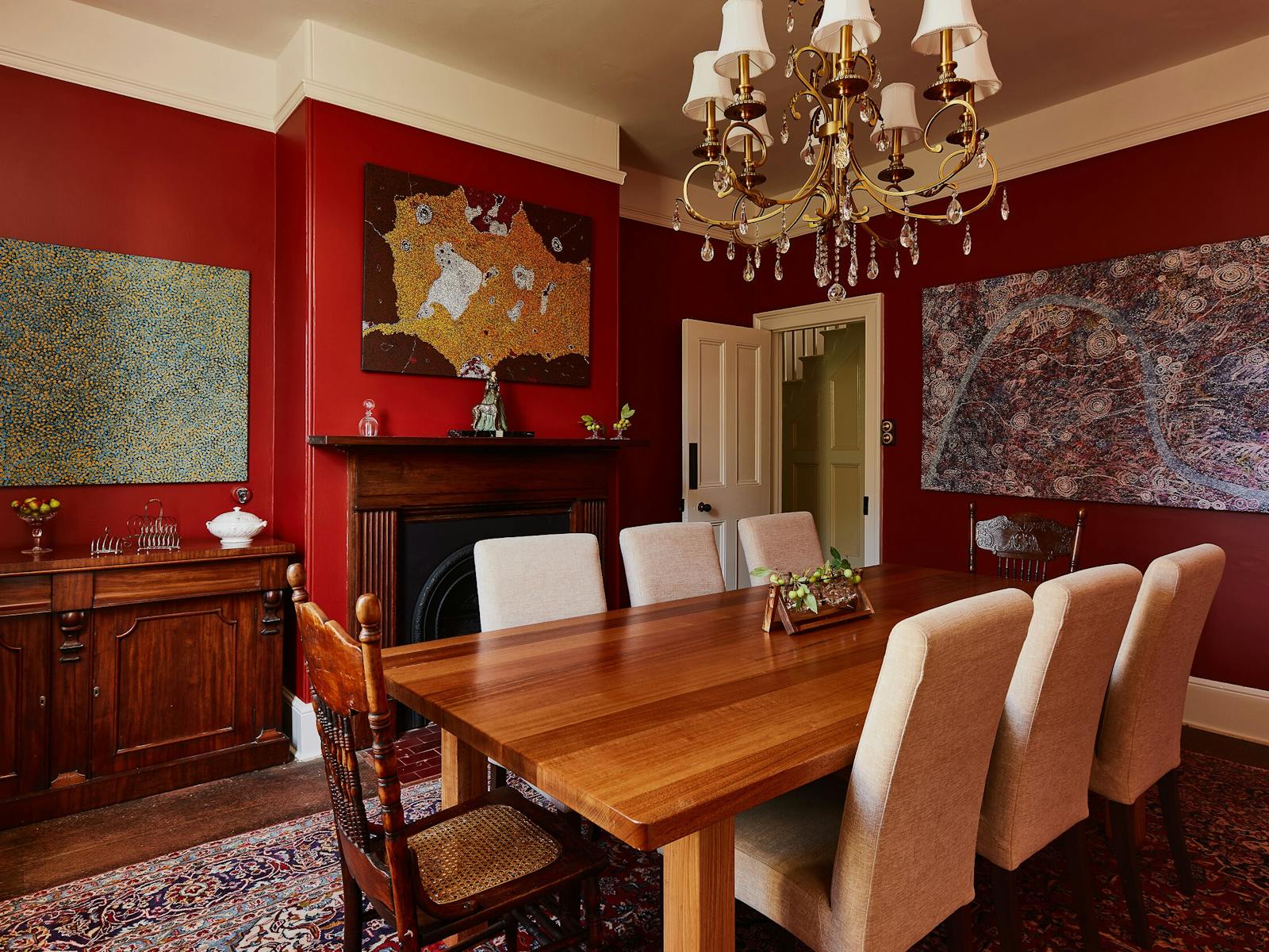 A large candelabra hangs over a 6 seat dining table. Eclectic art hangs on the red walls.