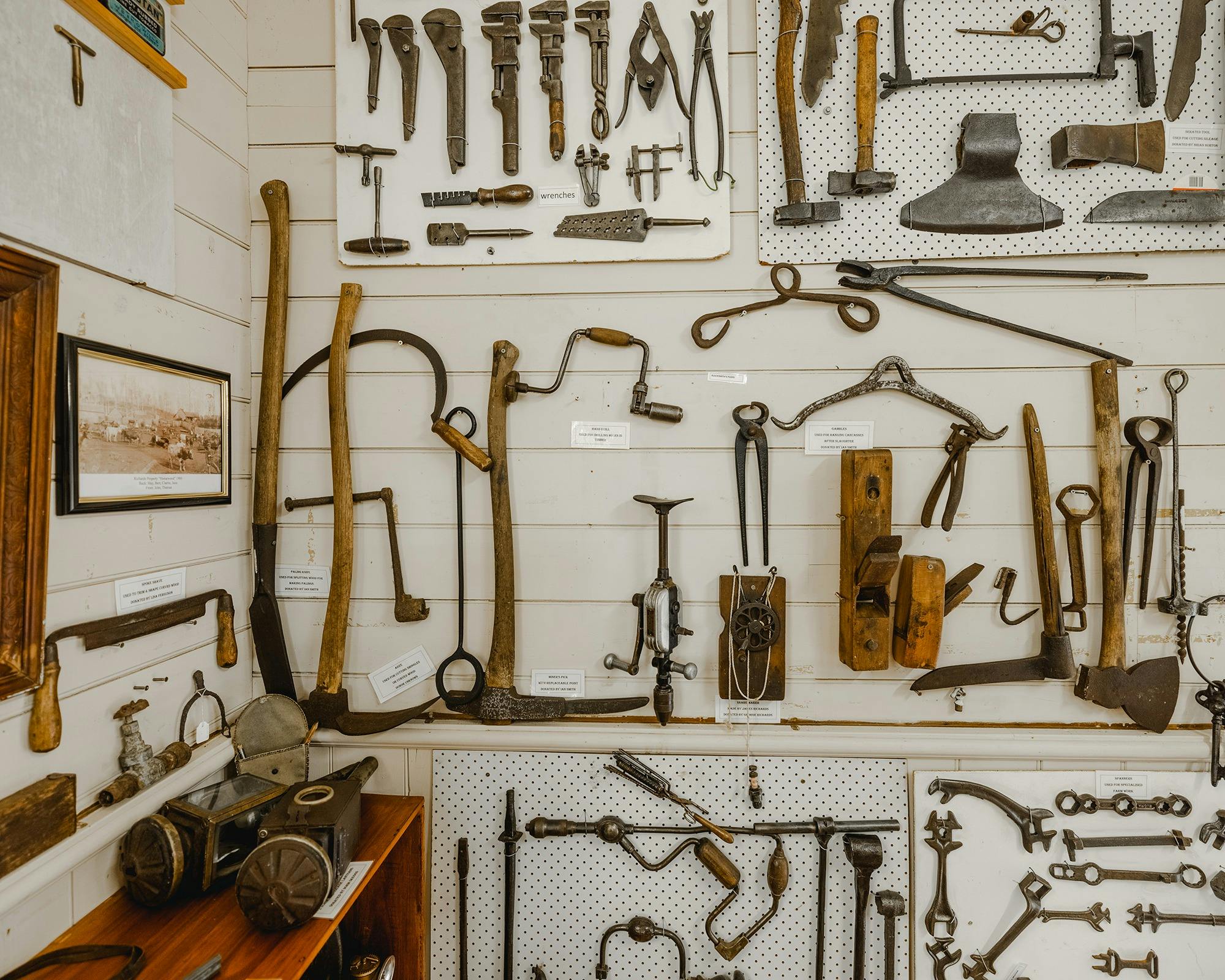Historic farming tools are hung artfully on a white wall