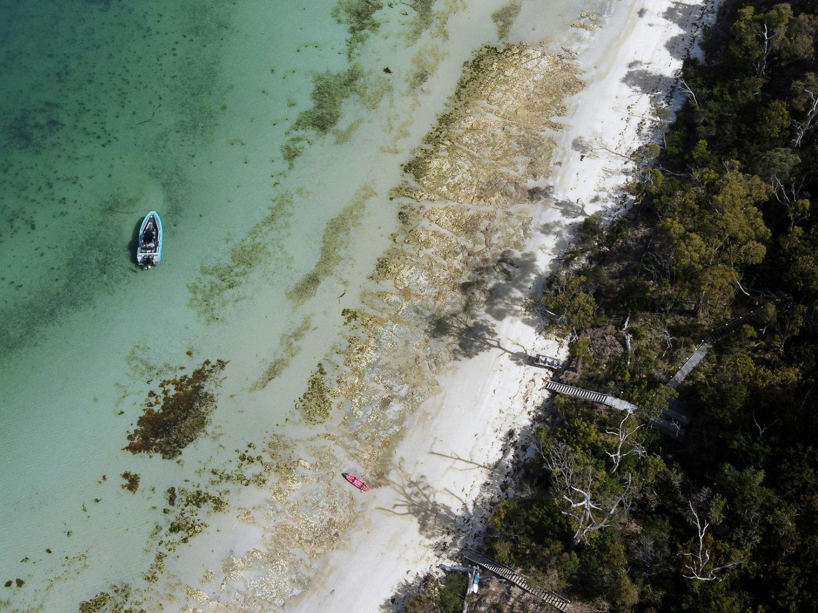 Aerial view of Islander vessel anchored beside a pristine sandy shore.