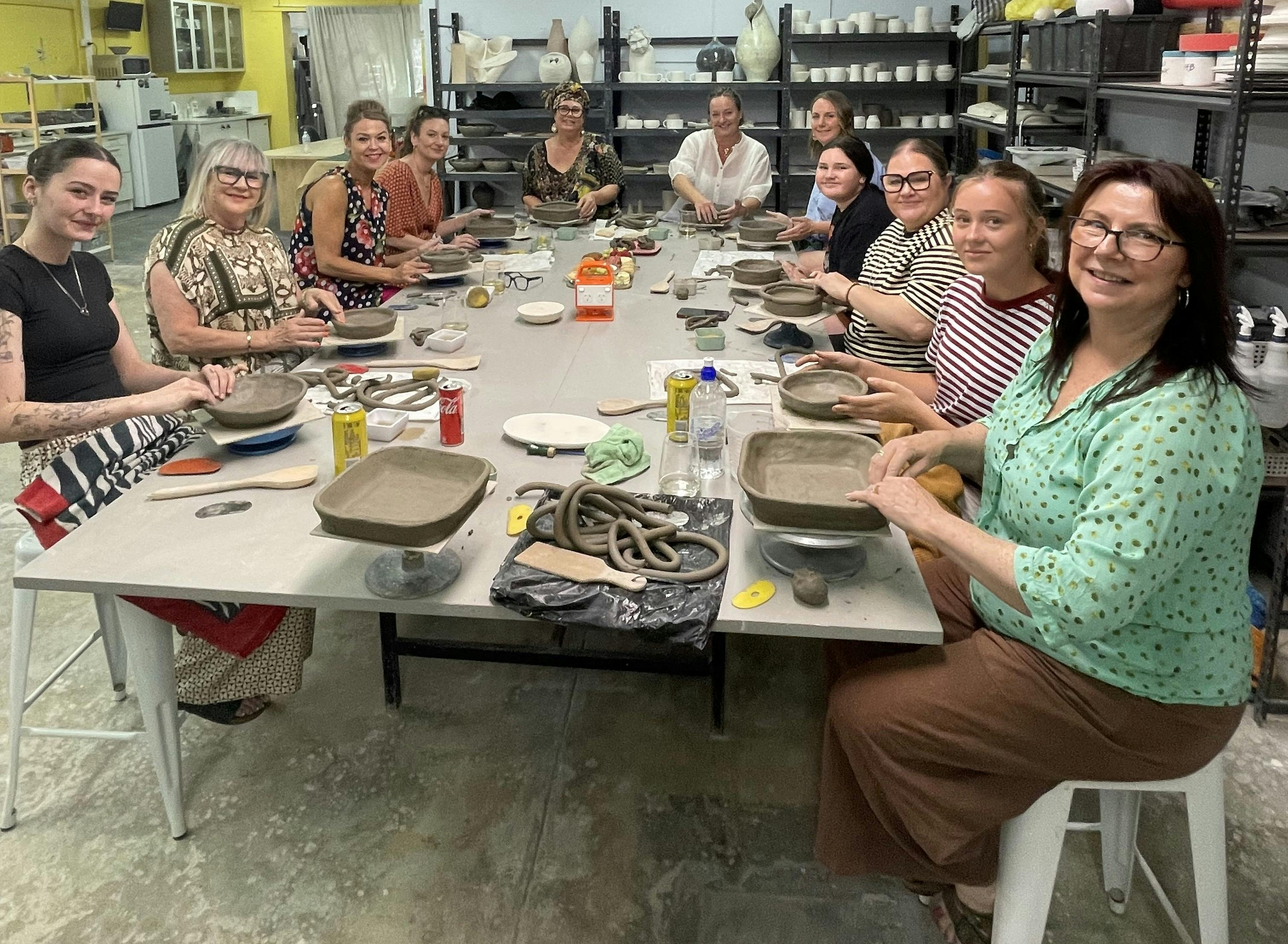People sitting around a table creating a pottery bowl using the coil method