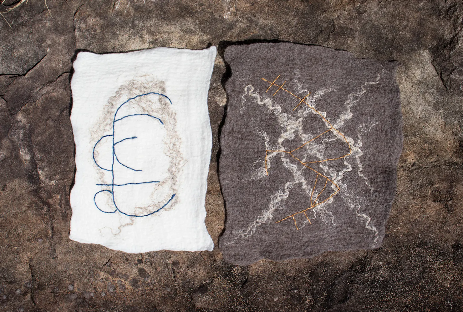A light piece of felt sits beside a dark brown piece of felt on a rock. Both pieces have patterns