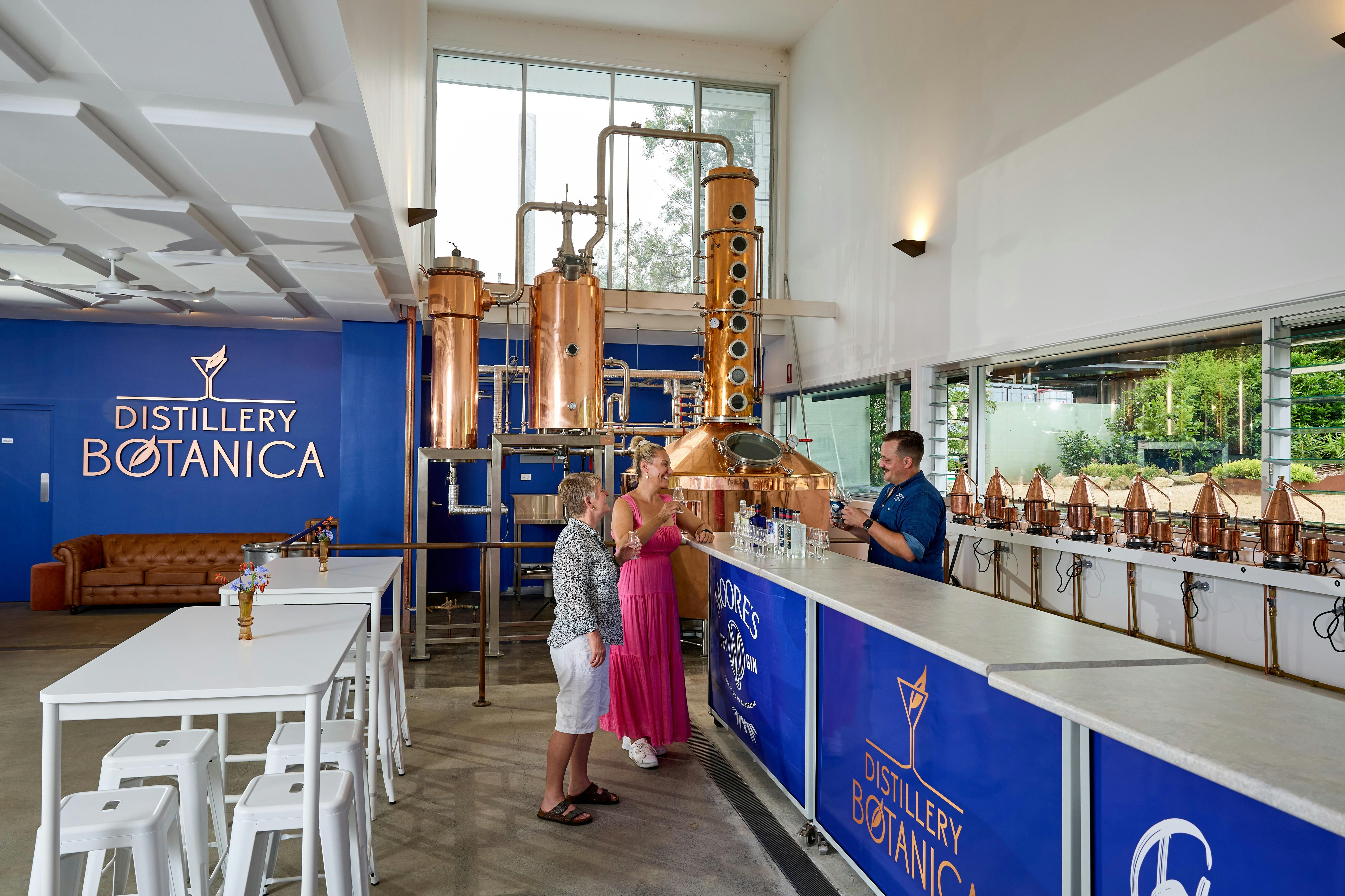 Visitors tasting gin at Distillery Botanica with copper stills and mini stills in the background