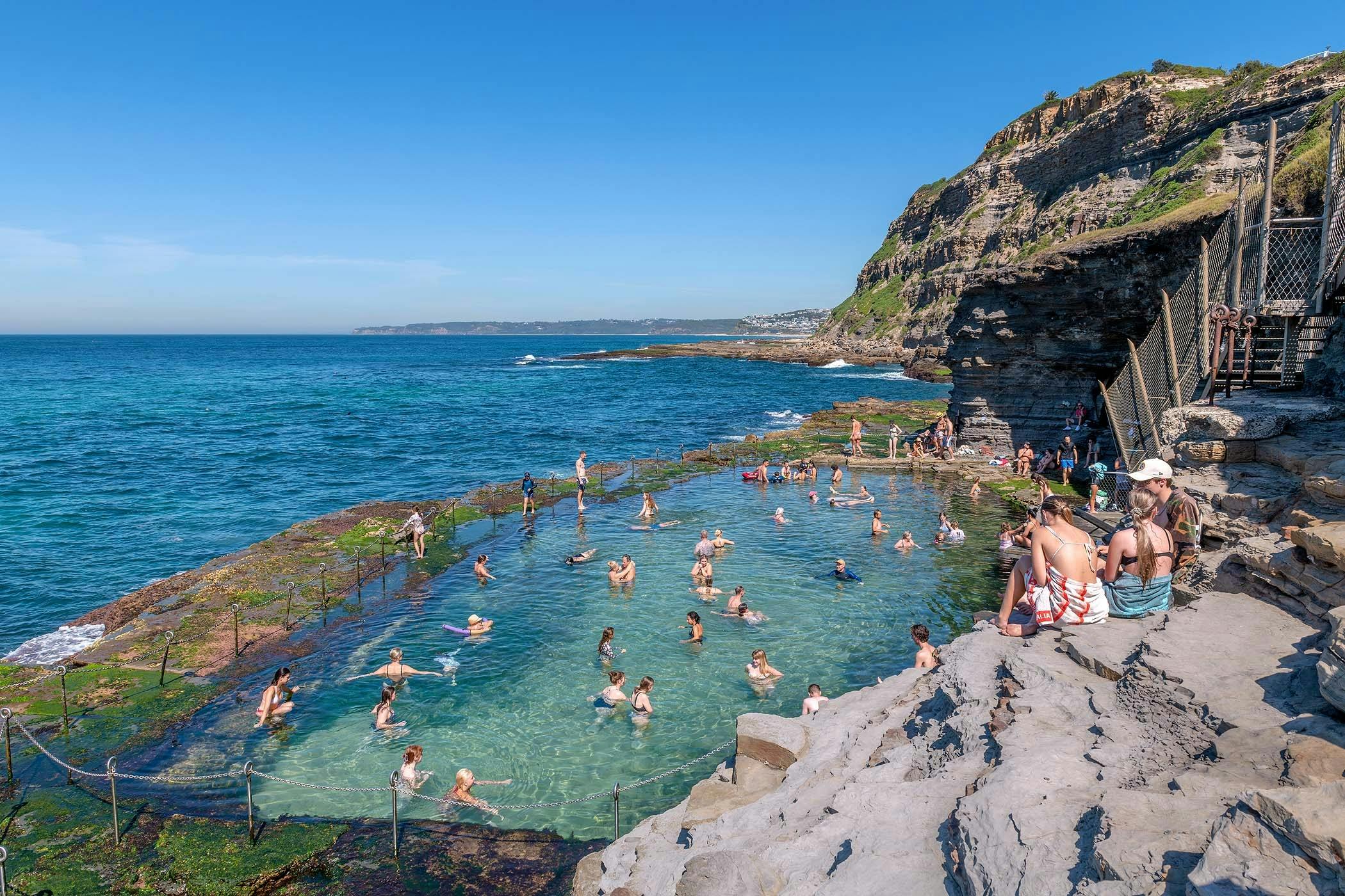 People swimming in the Bogey Hole ocean pool in Newcastle NSW with rock platform and ocean surrounds