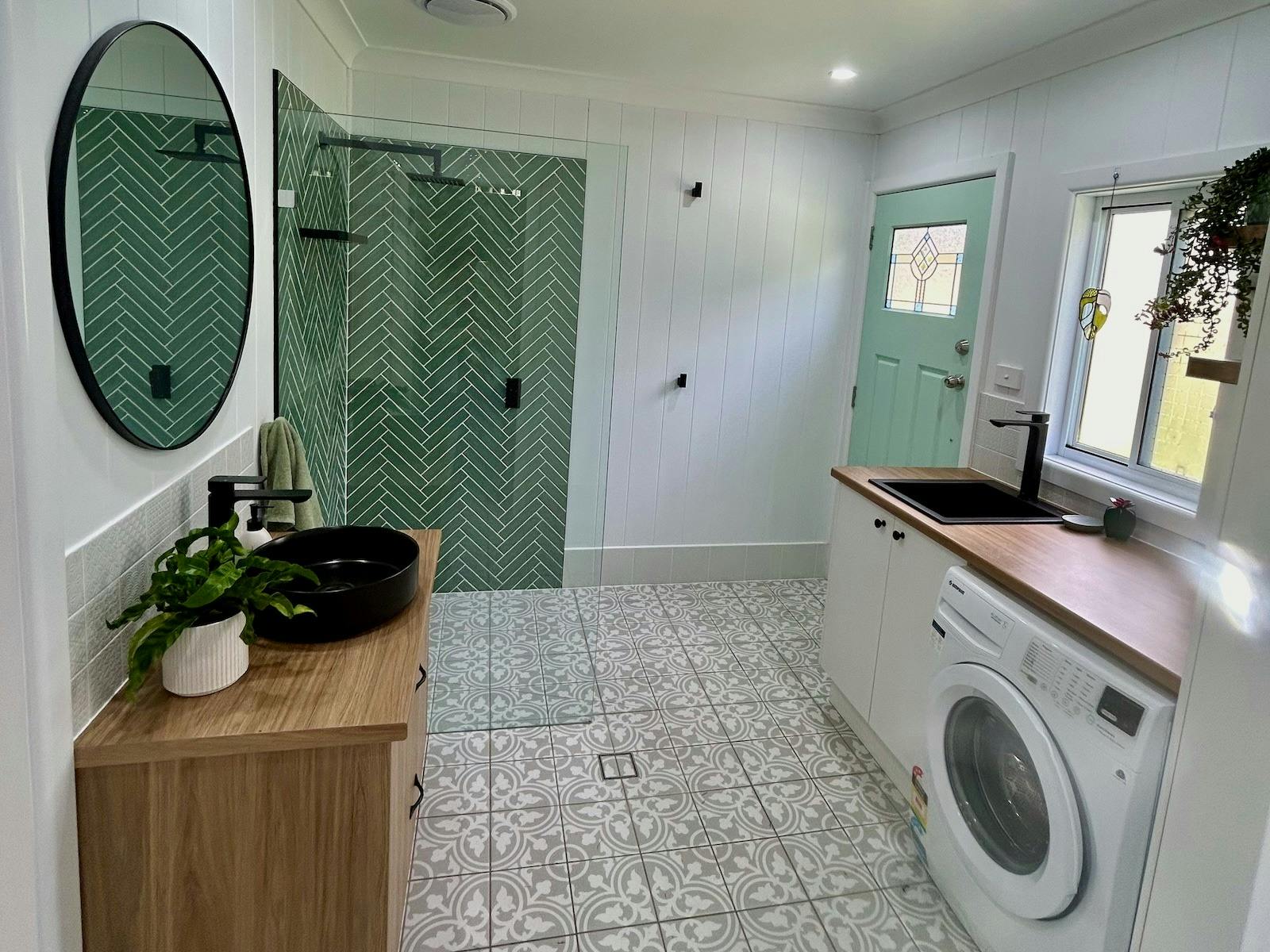 A modern laundry with a patterned tile floor, a green herringbone-tiled shower, and a blue door.