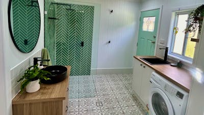 A modern laundry with a patterned tile floor, a green herringbone-tiled shower, and a blue door.