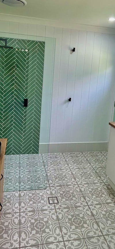 A modern laundry with a patterned tile floor, a green herringbone-tiled shower, and a blue door.