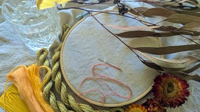 An embroidery hoop and thread next to a gin and tonic