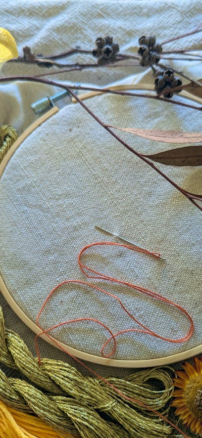 An embroidery hoop and thread next to a gin and tonic
