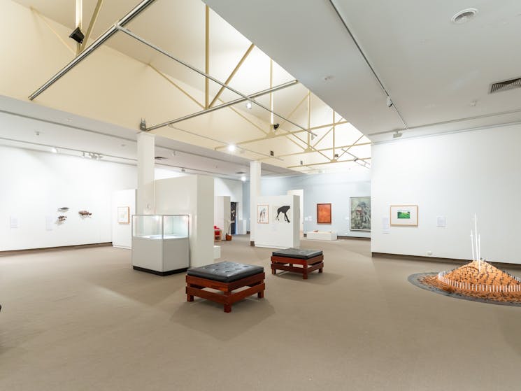 The image shows a light filled gallery with works from the permanent collection and local artists.