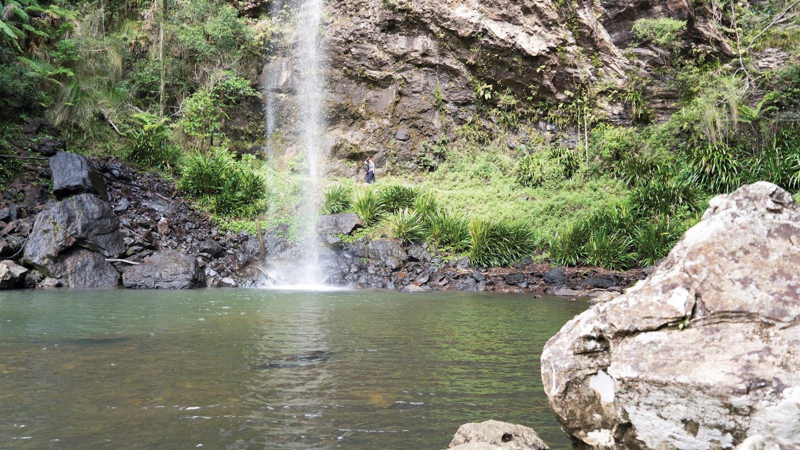 Two people walking behind a waterfall.