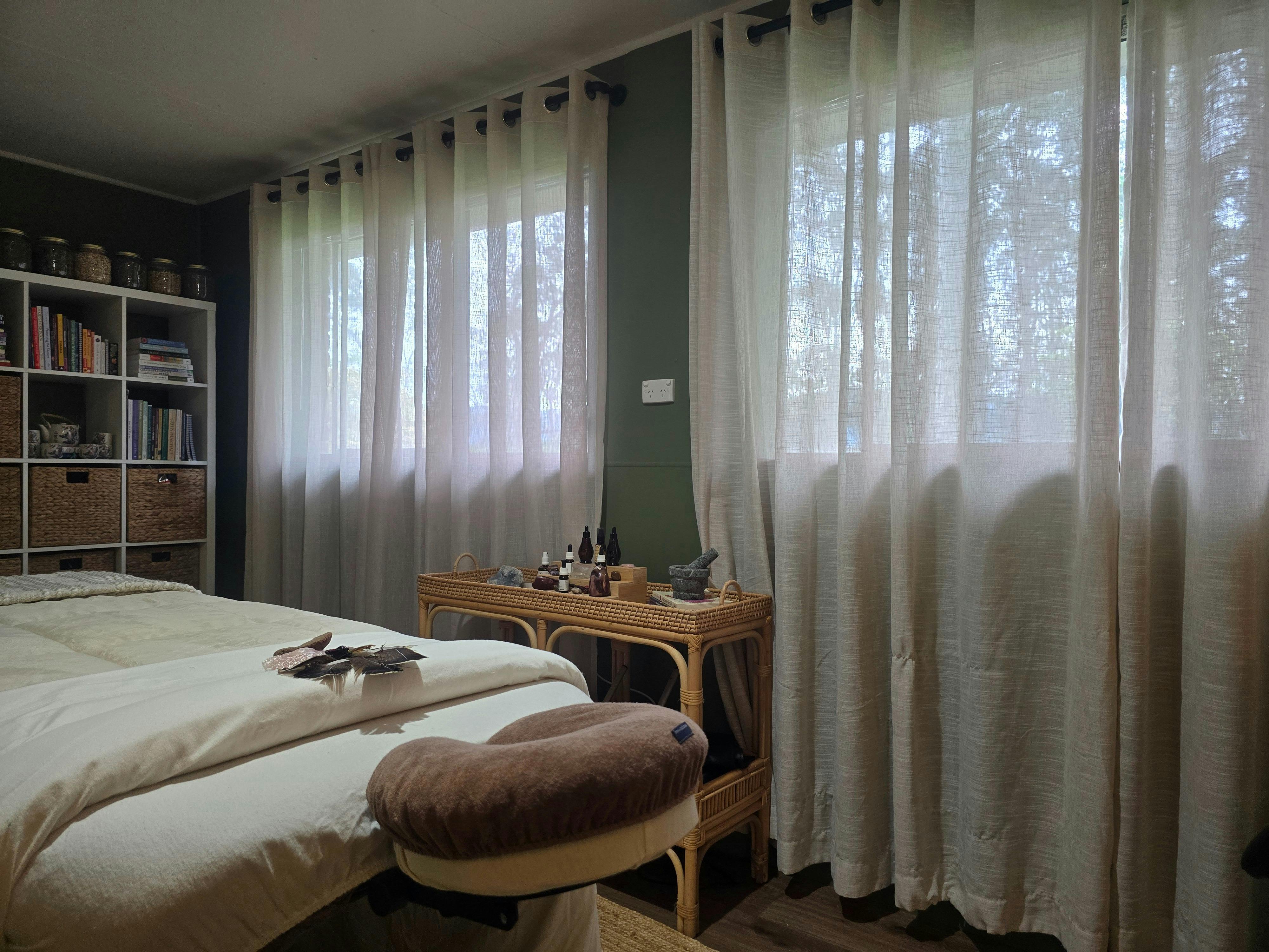 Warm women’s treatment room with massage table, natural textures, soft lighting, herbal decor.