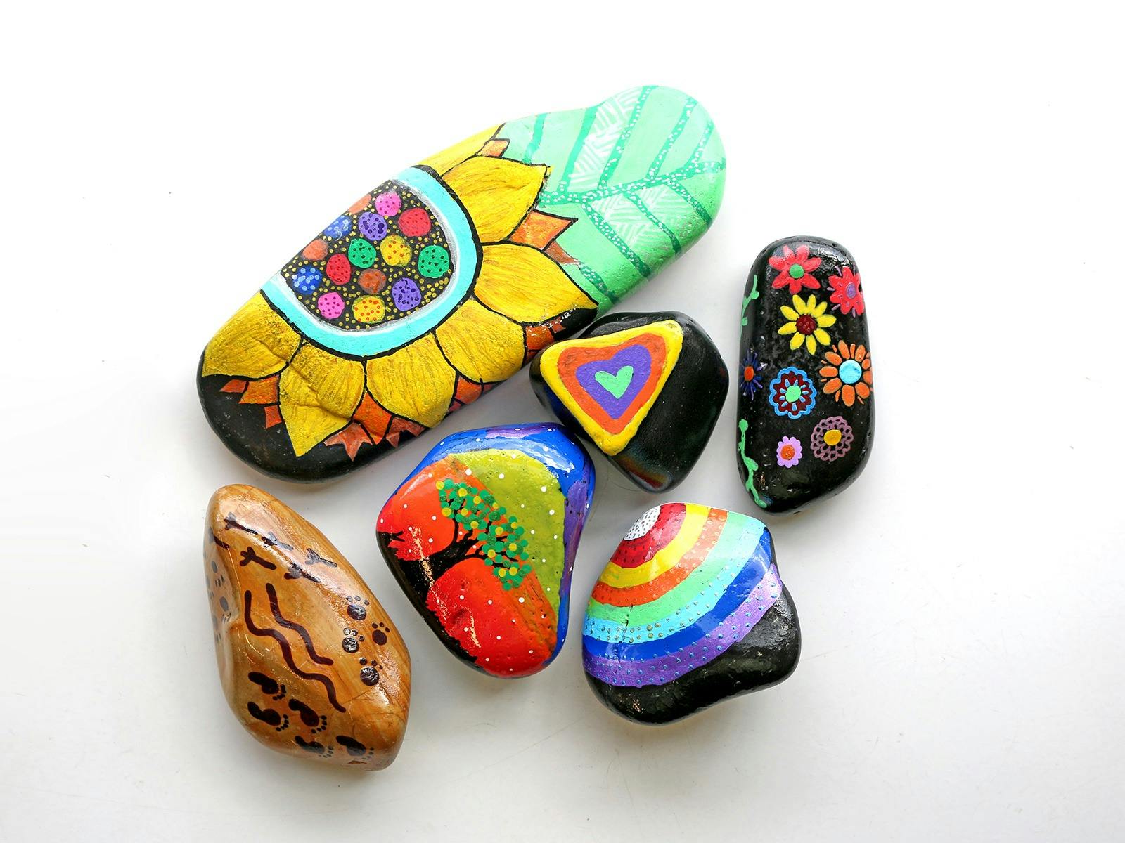 River rocks decorated in brightly coloured hand drawn images of flowers, trees, rainbows and pattern