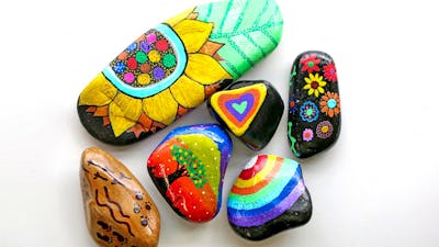River rocks decorated in brightly coloured hand drawn images of flowers, trees, rainbows and pattern