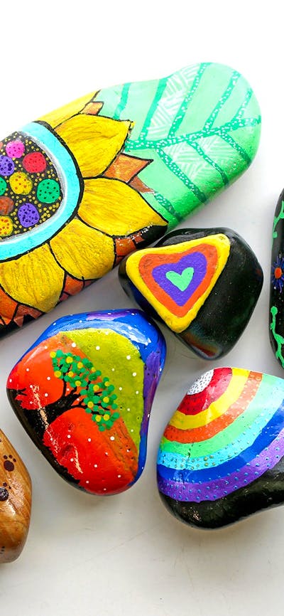 River rocks decorated in brightly coloured hand drawn images of flowers, trees, rainbows and pattern