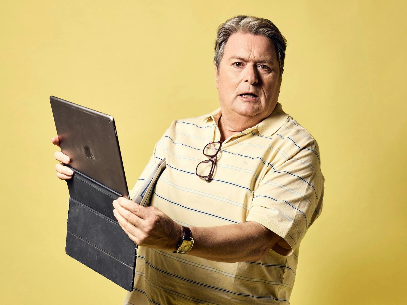 An older man in a yellow striped polo shirt holds a tablet and stylus