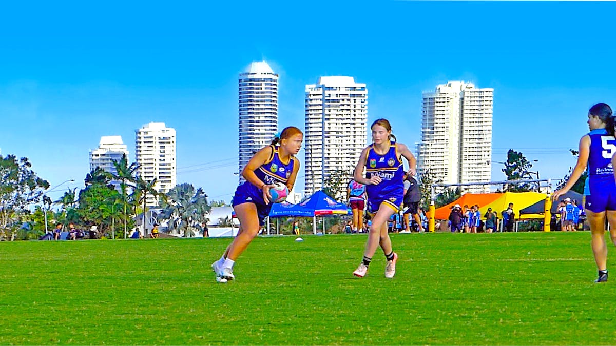 Young female touch players on a grassy field with the Gold Coast city skyline in the background