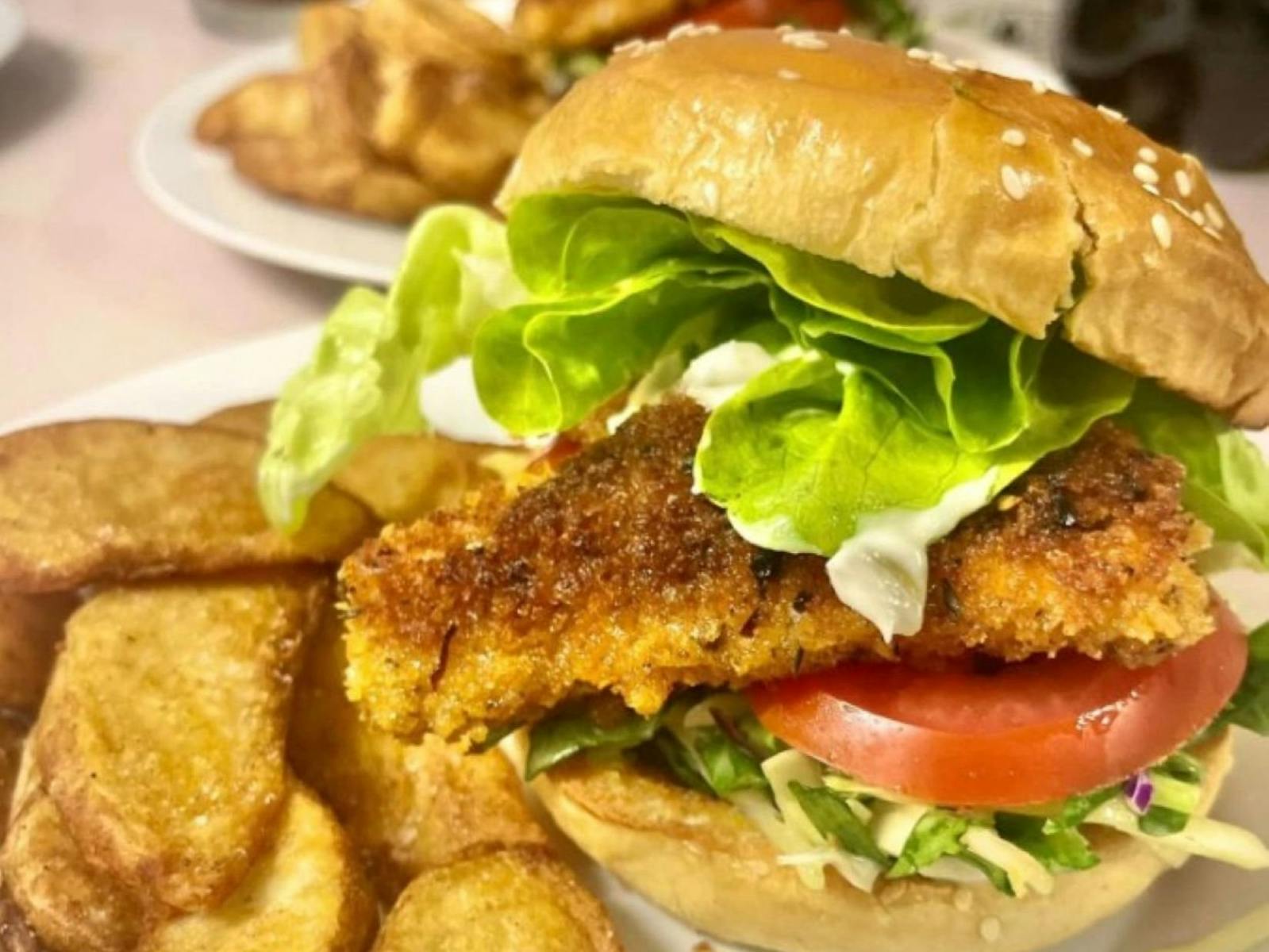 A crumbed fish burger with fried wedges on the side