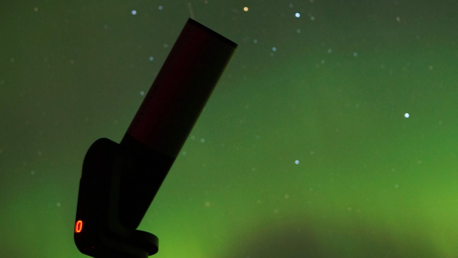 Telescope set up beneath a glowing aurora on a clear Tasmanian night.
