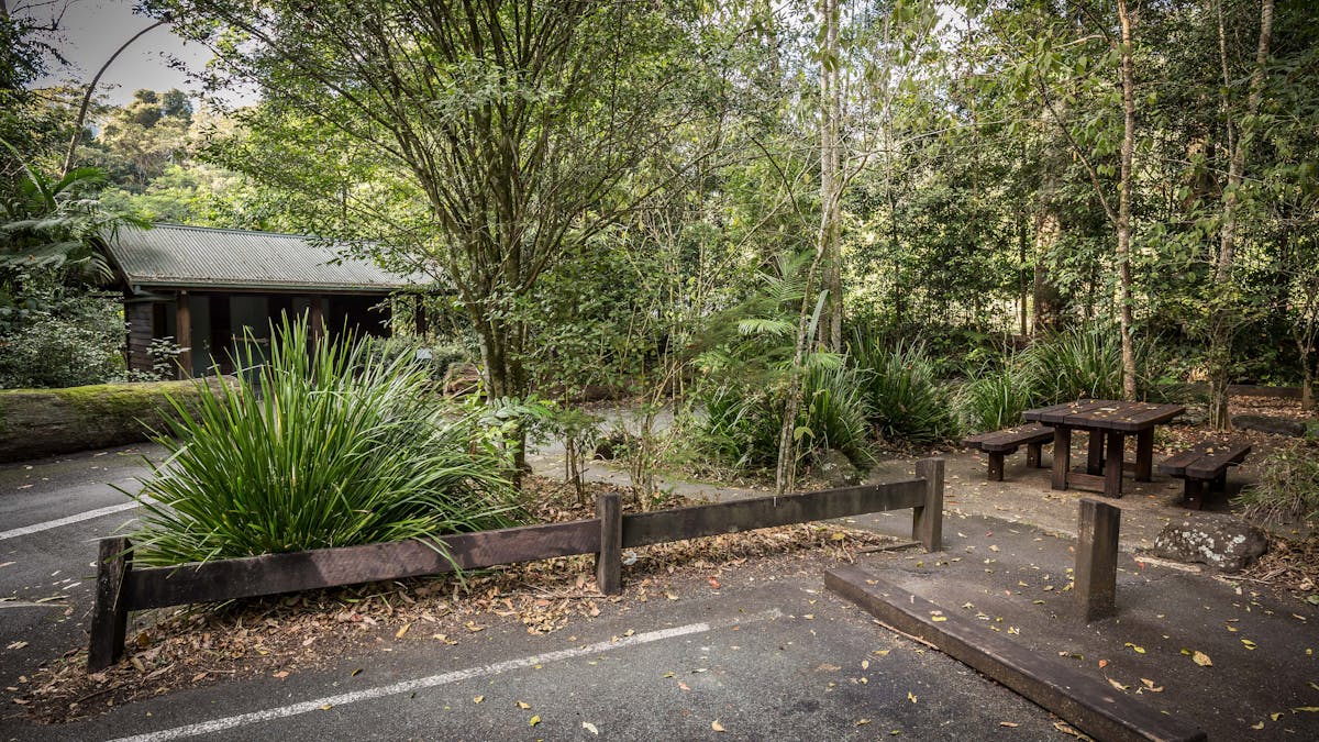 Toilets in the background, wooden picnic table on the right and a car park in the foreground.