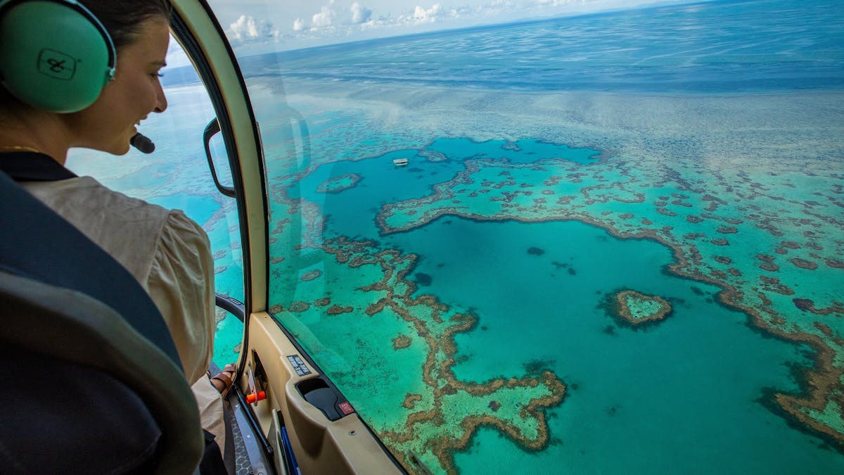 Aerial view from helicopter showing pilot looking down on heart reef and surrounding coral in sea
