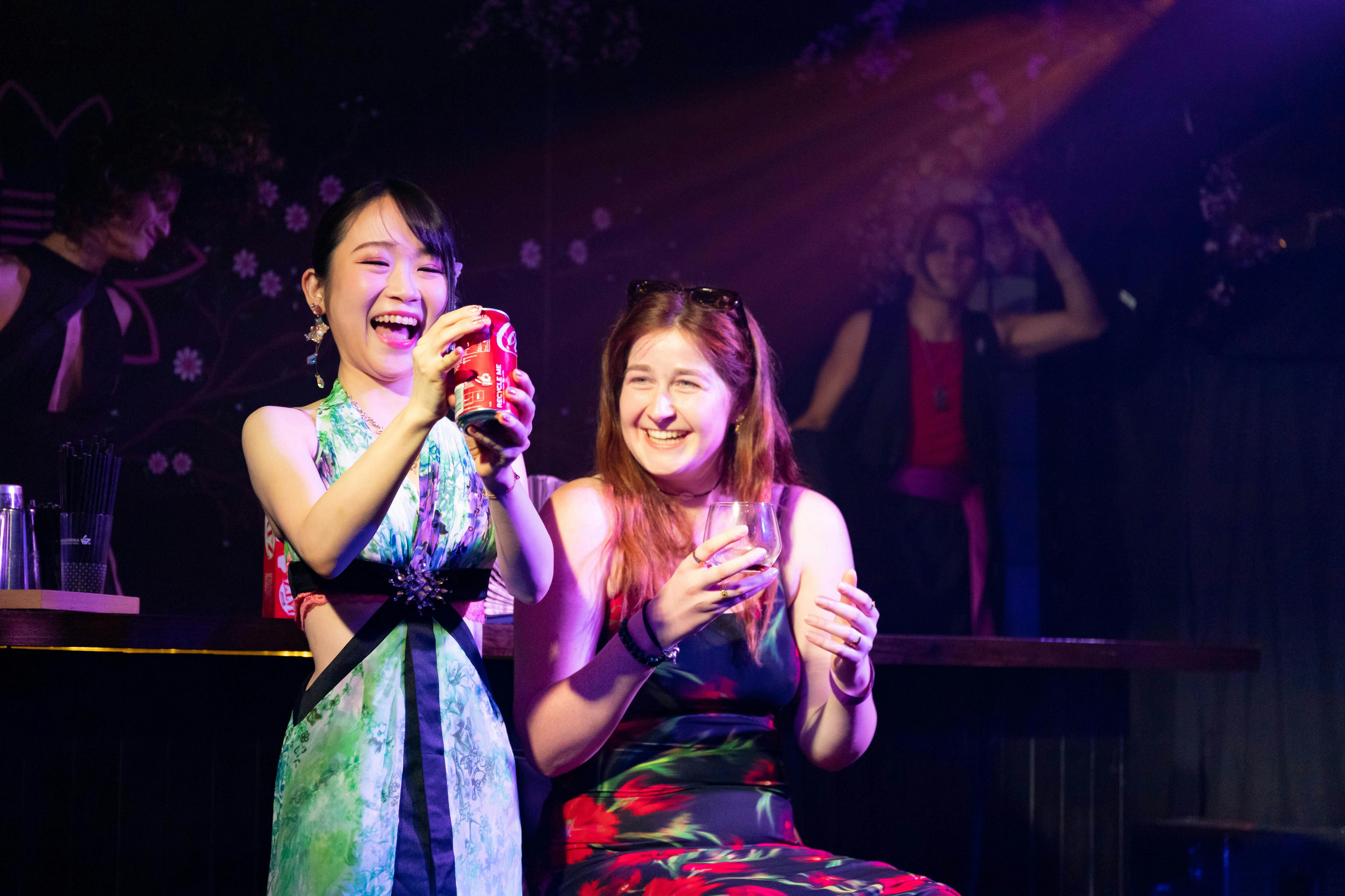 A magician is smiling holding a coke can in front of her, and audience member sits right beside her