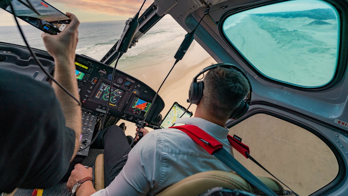 Inflight action shot of the Airbus H125 overhead a beach at sunset featuring bose A20 headsets.