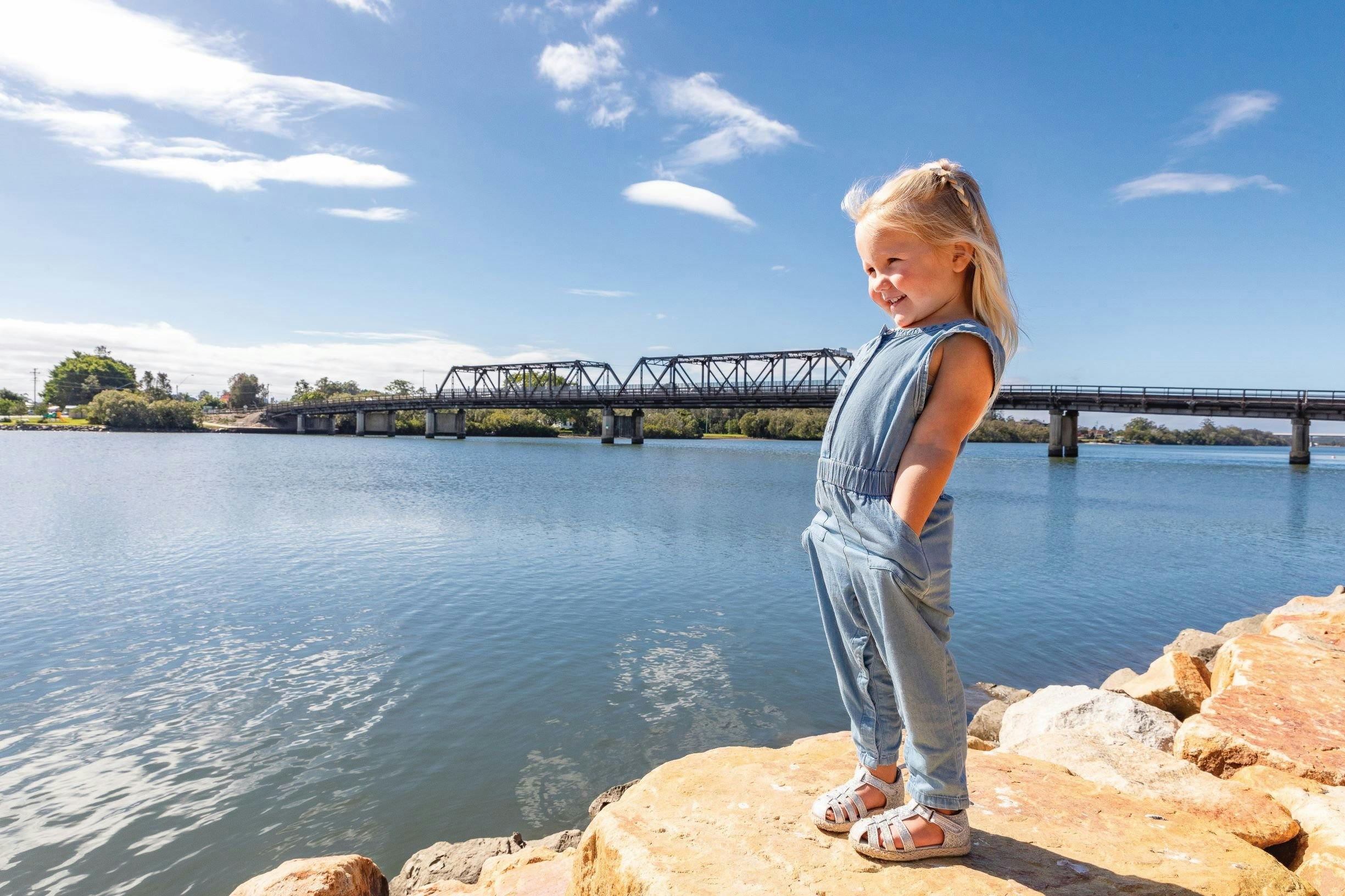 Little girl on the riverside with Macksville Bridge in background