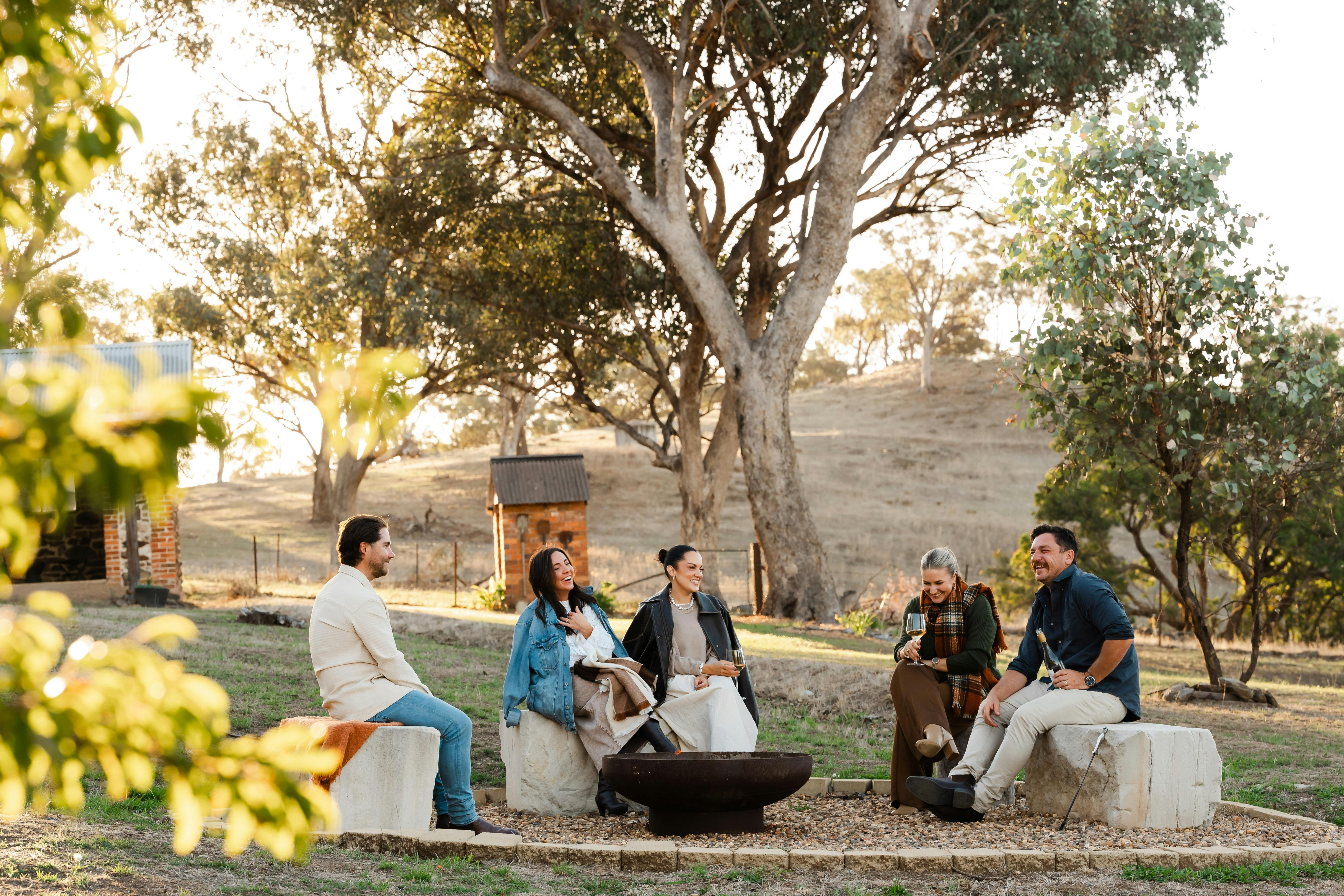 Group of friends, 3 women and 2 men, enjoying time around the firepit in the late afternoon sunshine