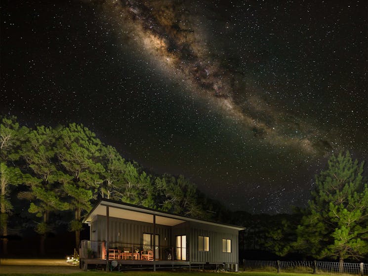 An image of Nightcap cottage sitting in a paddock at night with the Milky Way arching over the top.