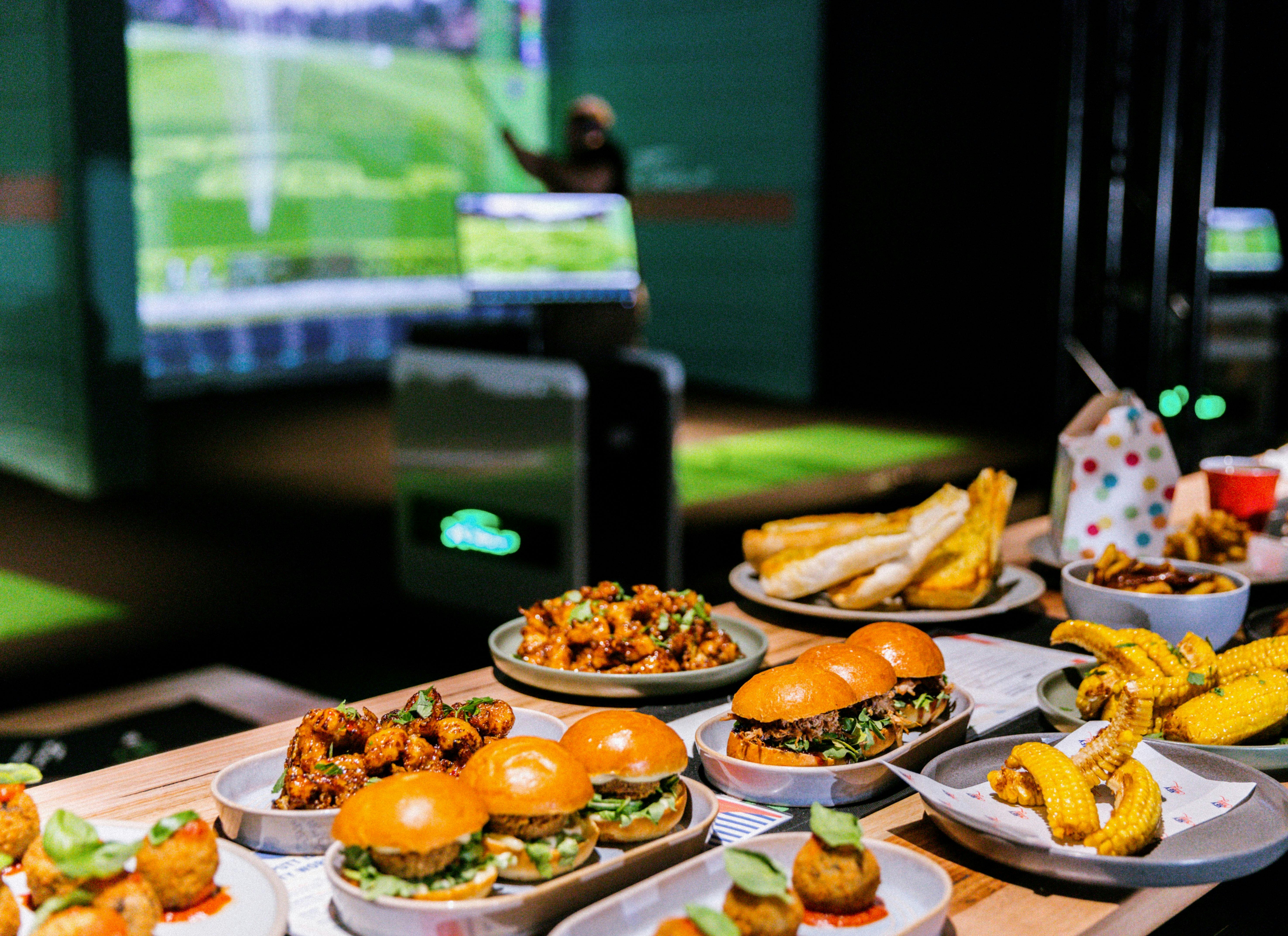 a delicious display of food including sliders, popcorn chicken and pizzas in front of the simulators
