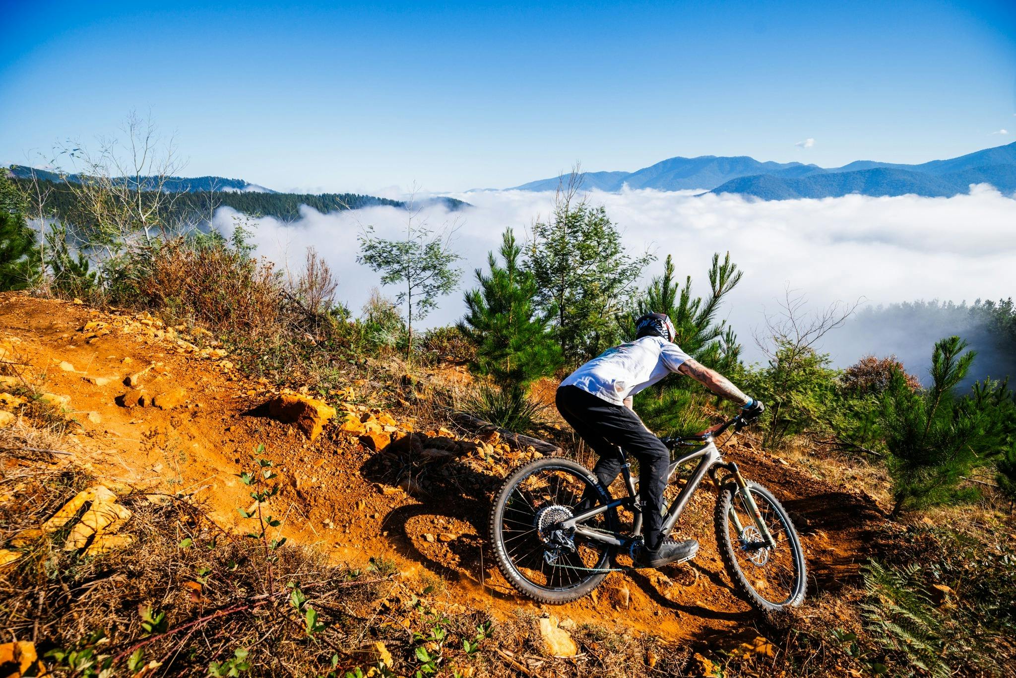 Rider on single trail with MTB and cloud inversion in mountain backdrop