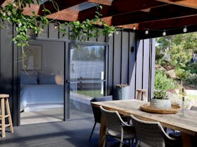 Outdoor entertaining area with dining table, lush greenery and sliding doors opening to a bedroom at