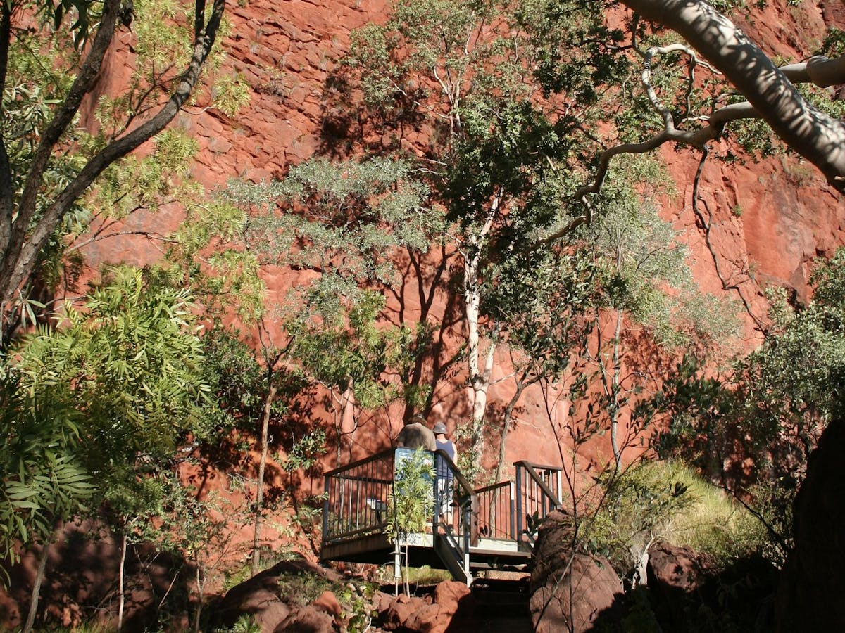 Two people standing on boardwalk platform in gorge looking at red rocky cliff face