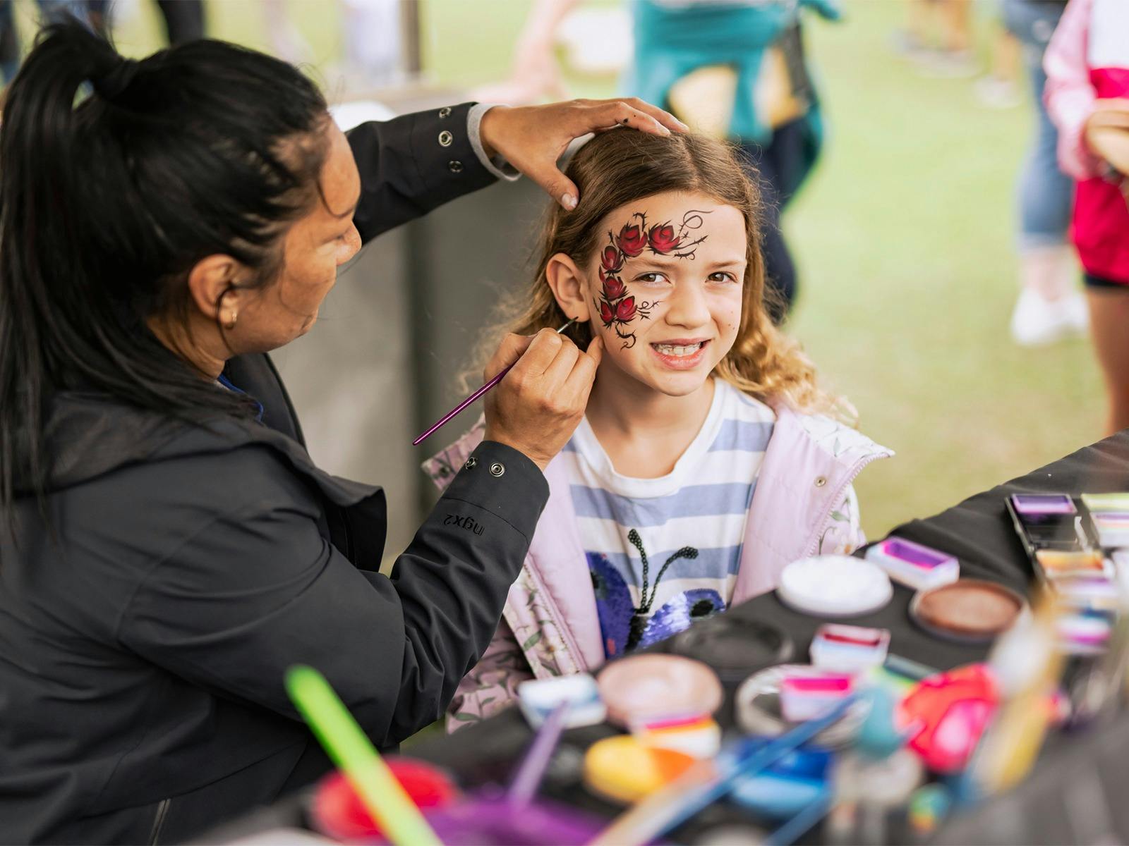 A young girl is getting her face painted with a floral design at Foundation Day