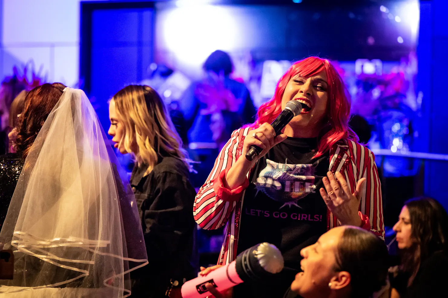 Women with pink hair and stripped pink jacket singing into a microphone