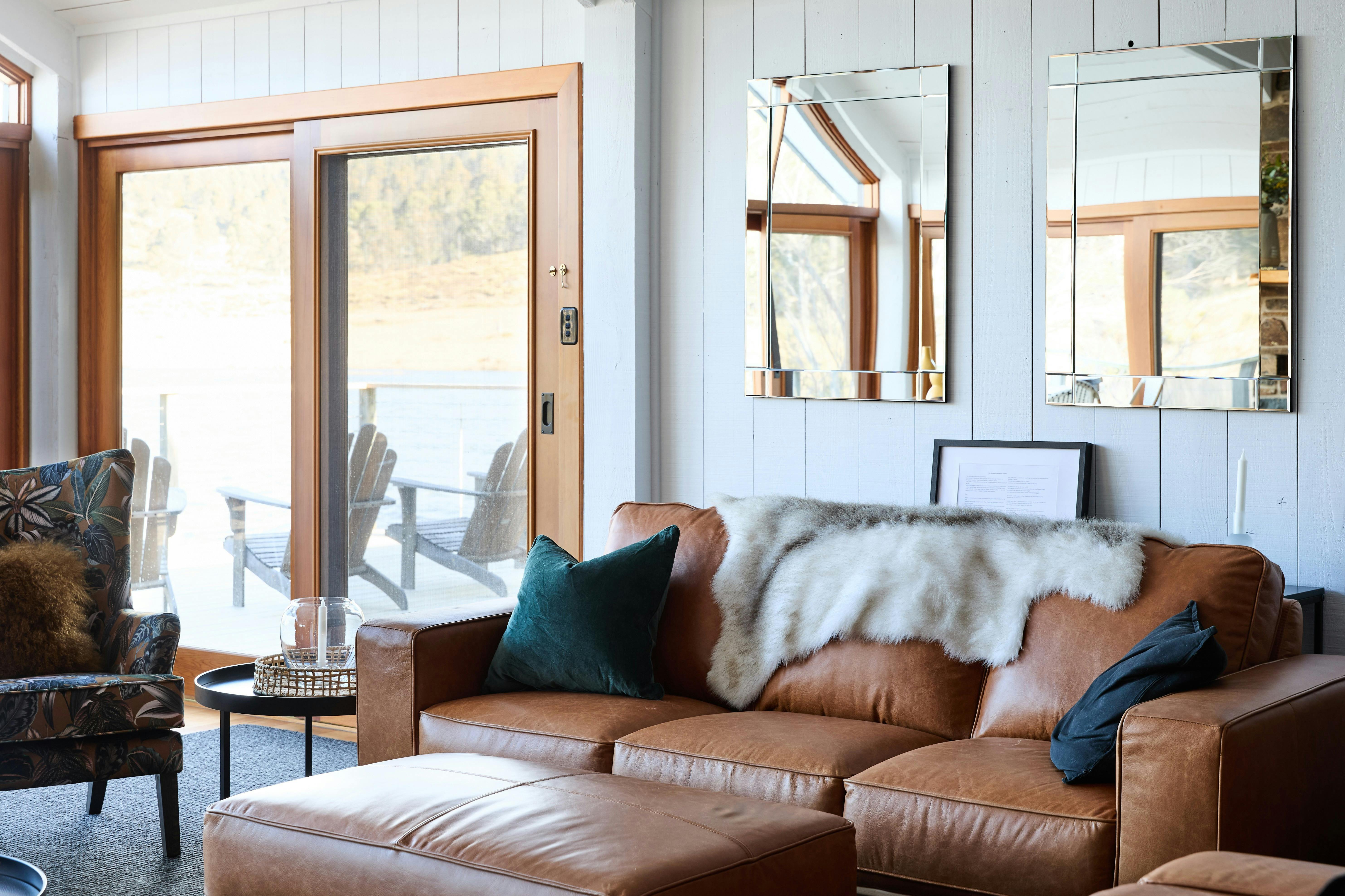 Tan leather couch in lounge room with glass doors onto deck with lake views