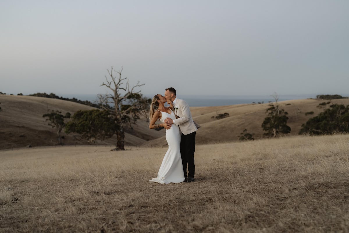 Wedding couple photo atop the rolling hills at Fleurieu Gin with ocean views in the background
