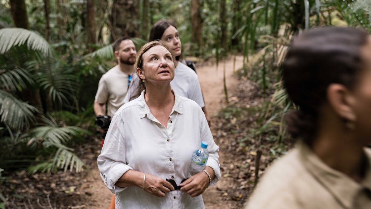 A women looking up to the tops of the trees while two people follow closely