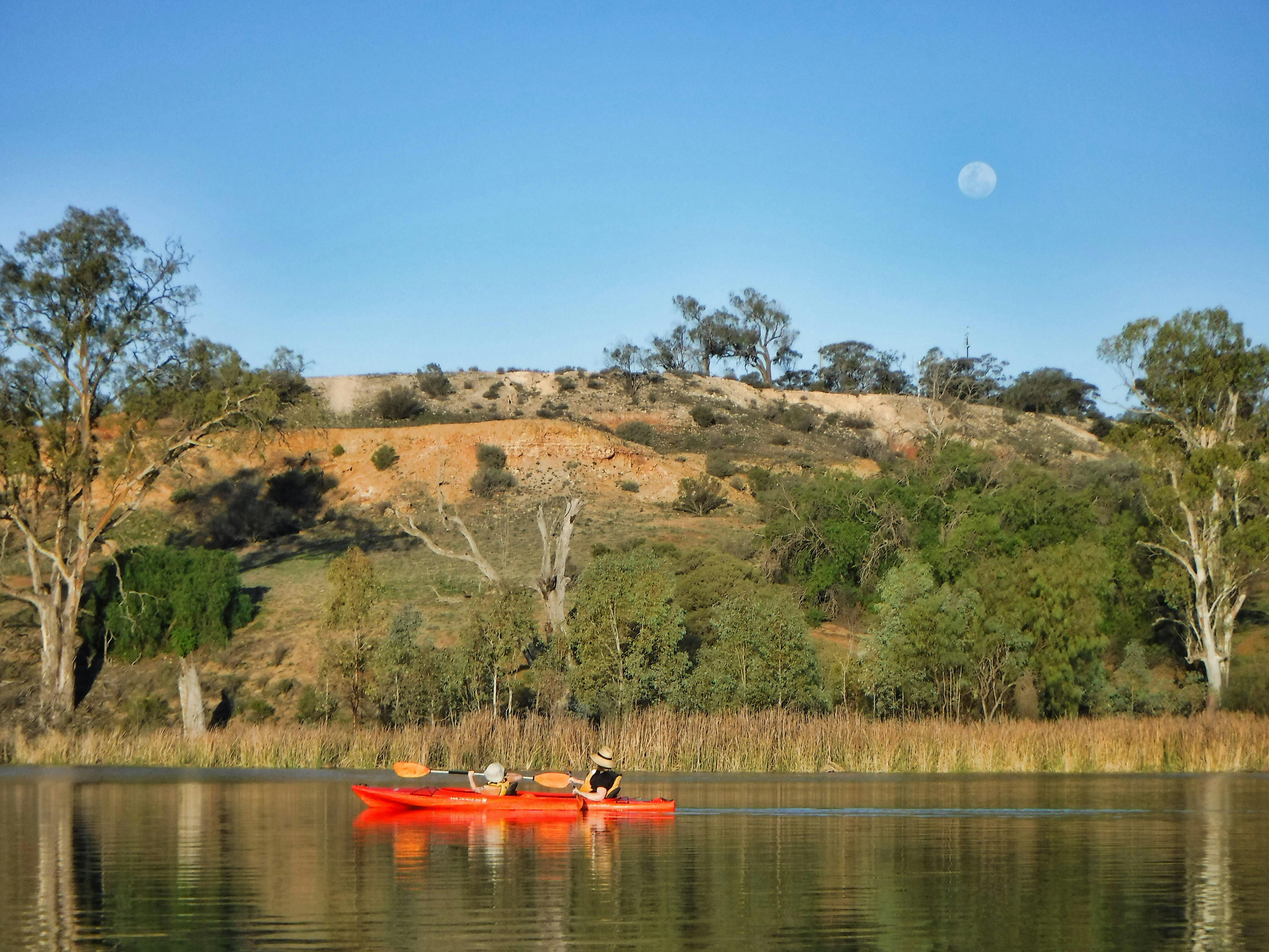 Mother and child in double kayak  ib a wetland lake in front of treed cliffs and a full moon