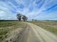 Gravel road with farms on either side trees in distance and blue sky with whispy clouds