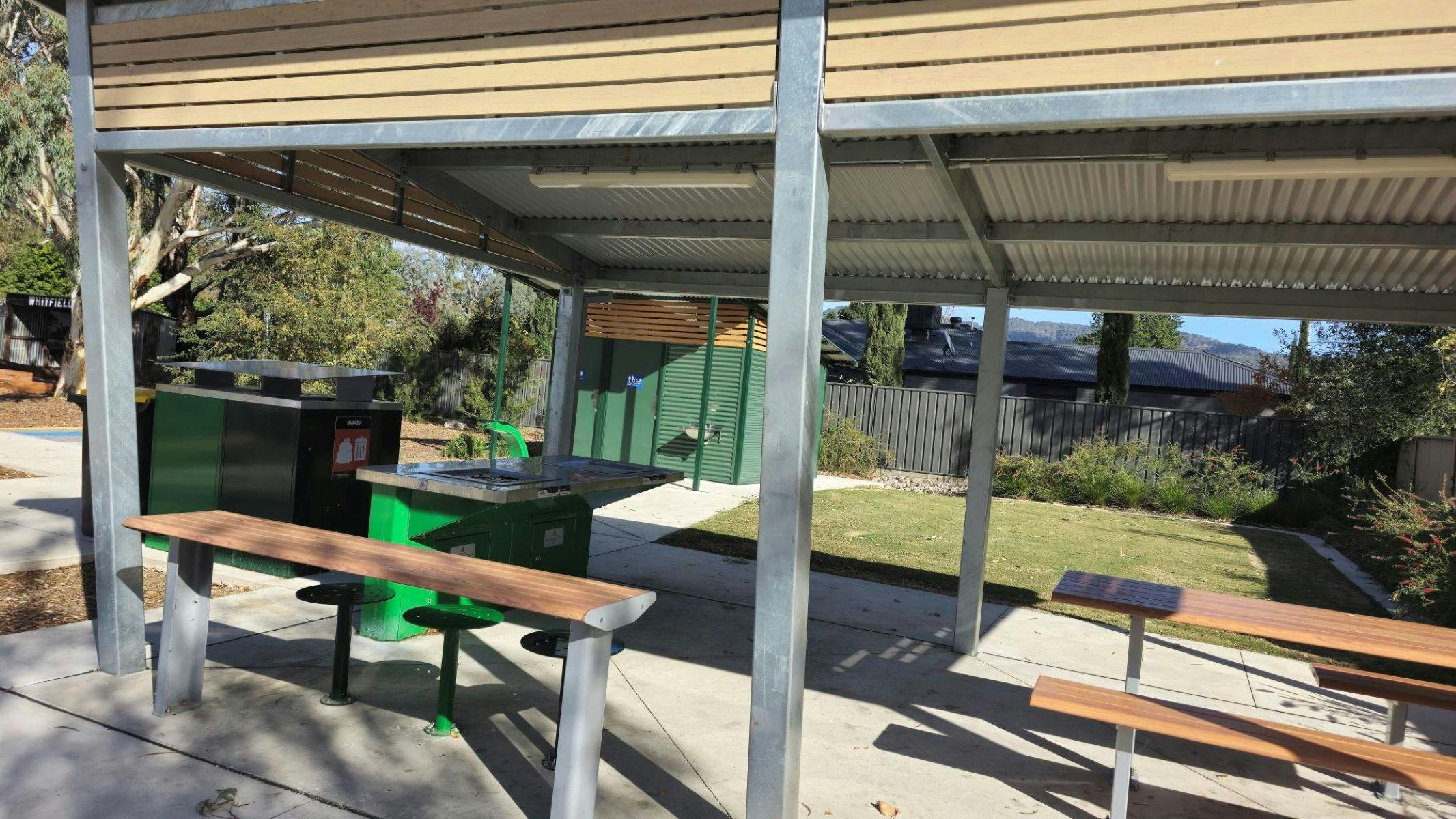 Shaded seating area with accessible tables and bbq. Green tin shed in background