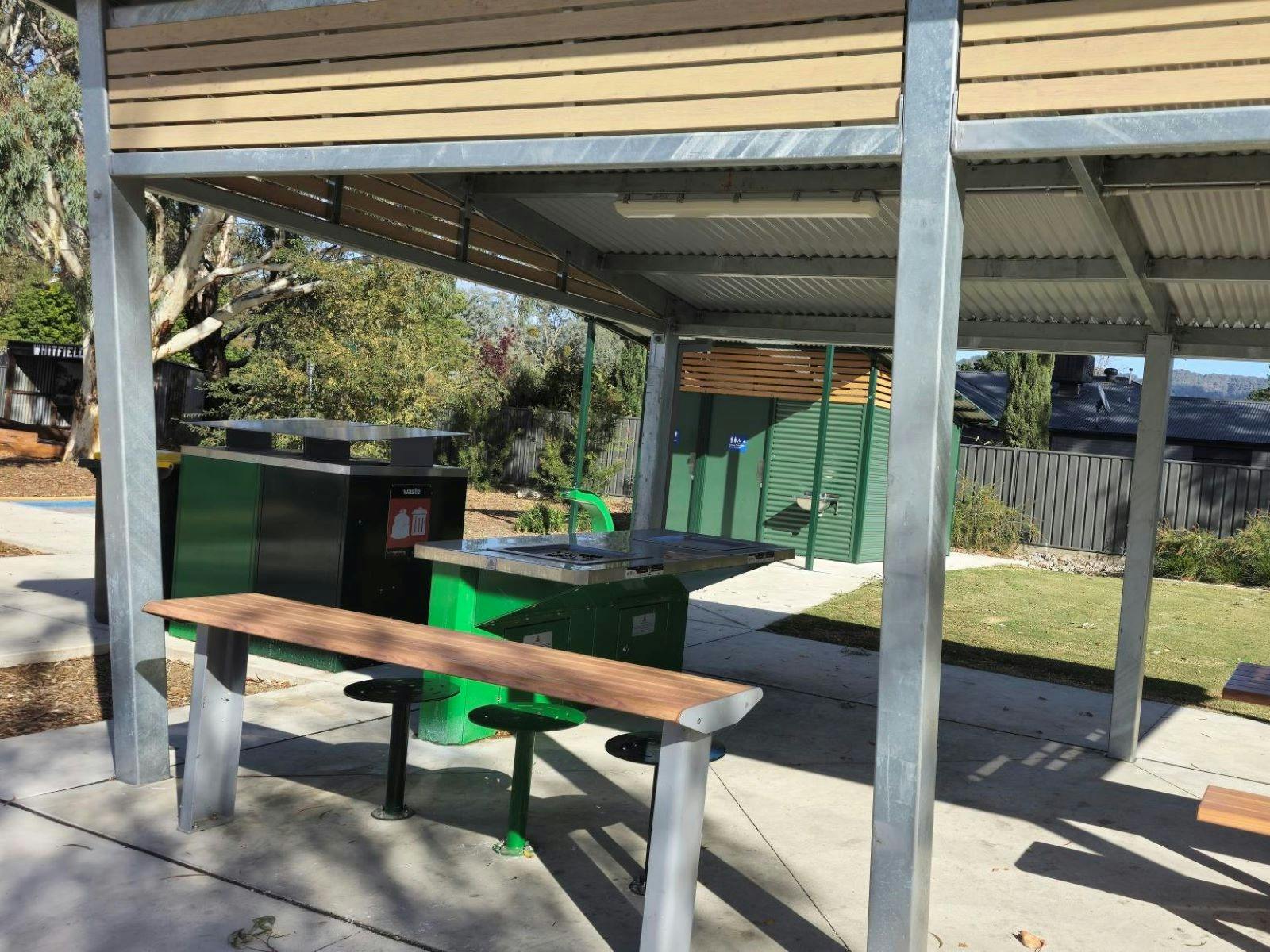 Shaded seating area with accessible tables and bbq. Green tin shed in background