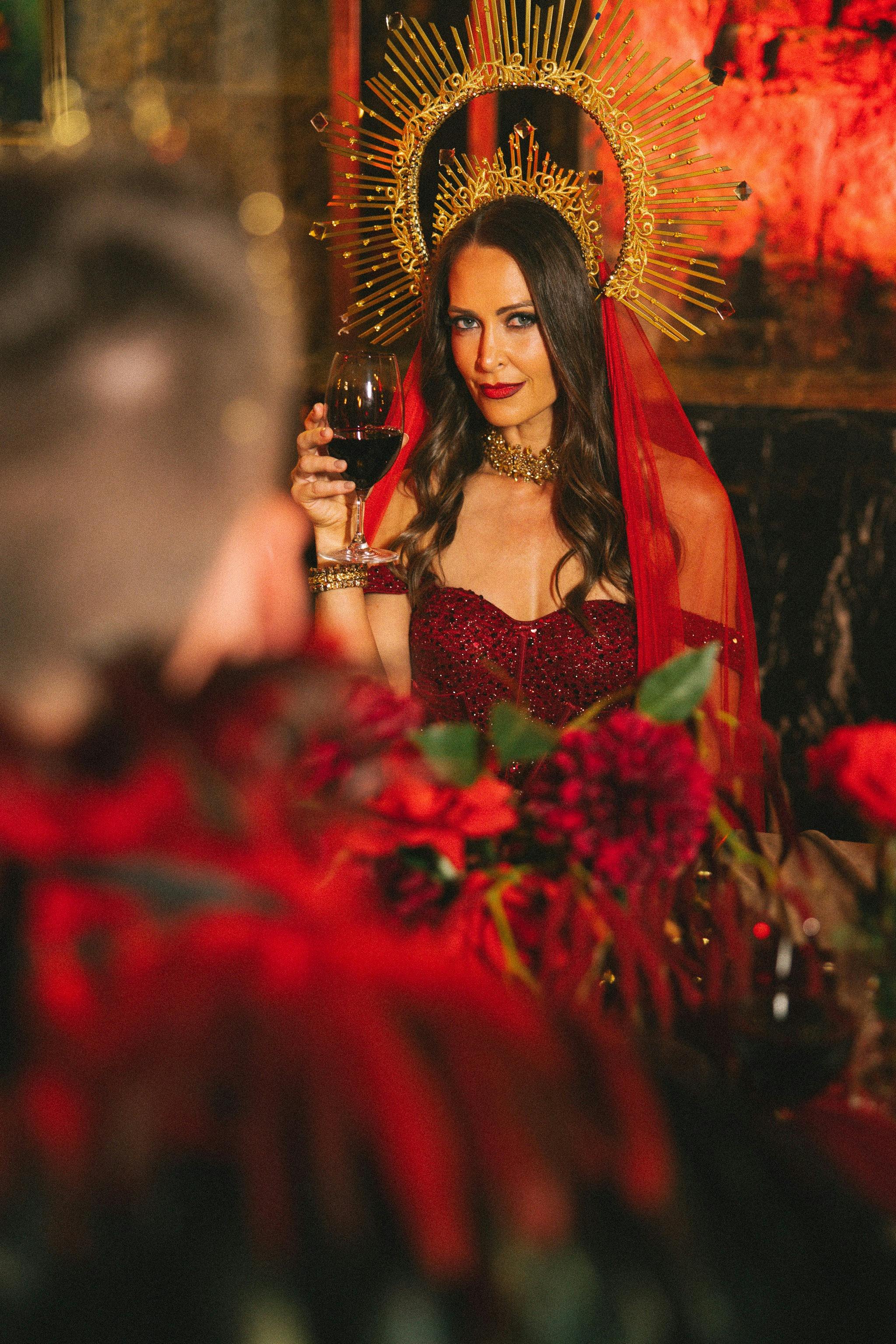 A character in a red dress toasting a glass of wine at a banquet table